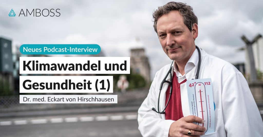 Foto von Eckart von Hirschhausen im Arztkittel mit einem symbolischen Fieberthermometer in der Hand. Im Hintergrund sieht man eine Straße und Häuser.