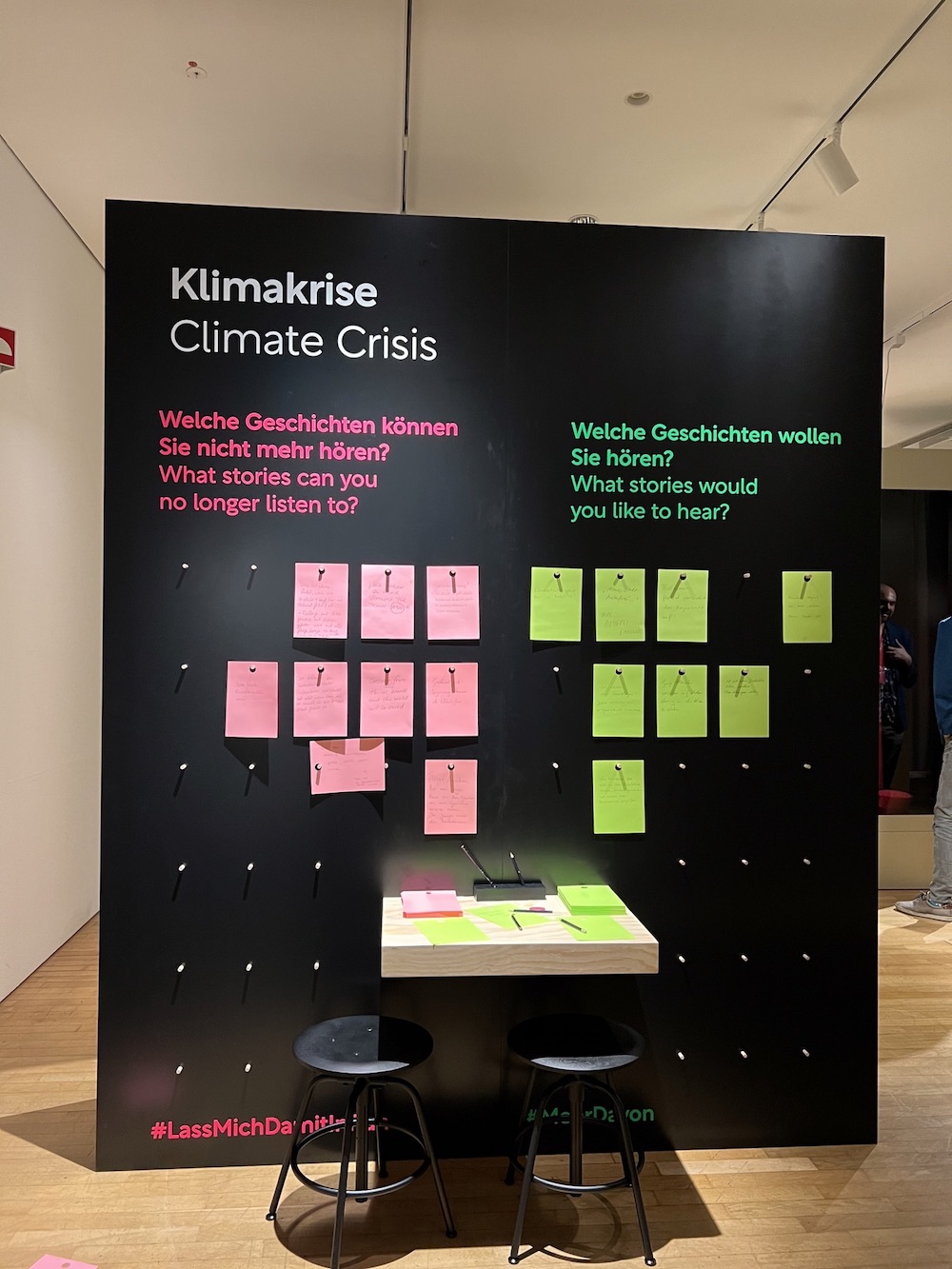 Schwarze Tafel auf der Klima_X Ausstellung mit persönlichen Fragen und Zetteln zur Stimmenabgabe, die an die Wand gepinnt werden können