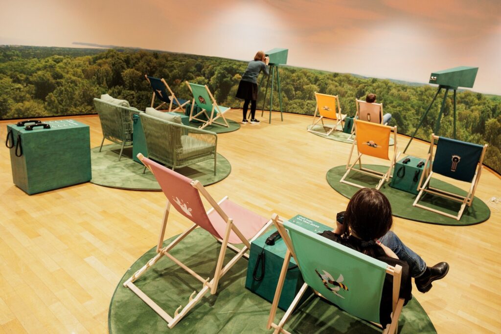 Foto von bunten Liegestühlen auf kleinen grünen Teppichinseln auf der KLIMA_X Ausstellung im Museum für Kommunikation Frankfurt