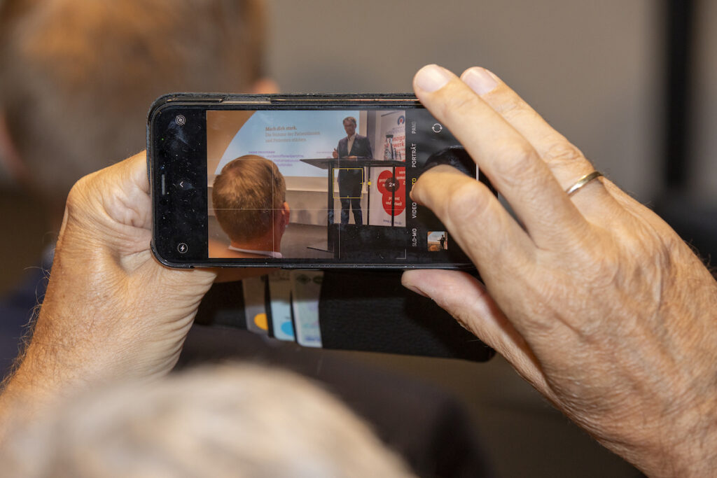 Foto eines Smartphones, mit dem eine Person ein Foto von der Aufktaktveranstaltung des Welttags der Patientensicherheit macht.