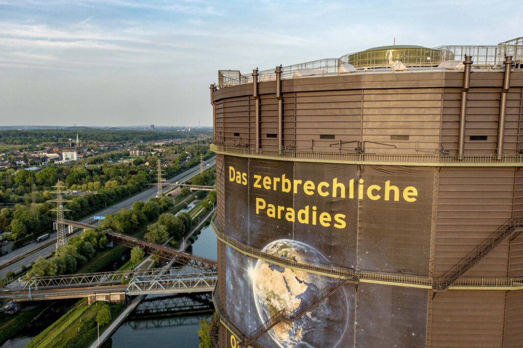 Foto des Gasometers Oberhausen mit Ausstellungsplakat "Das zerbrechliche Paradies", auf dem eine Weltkugel zu sehen ist.