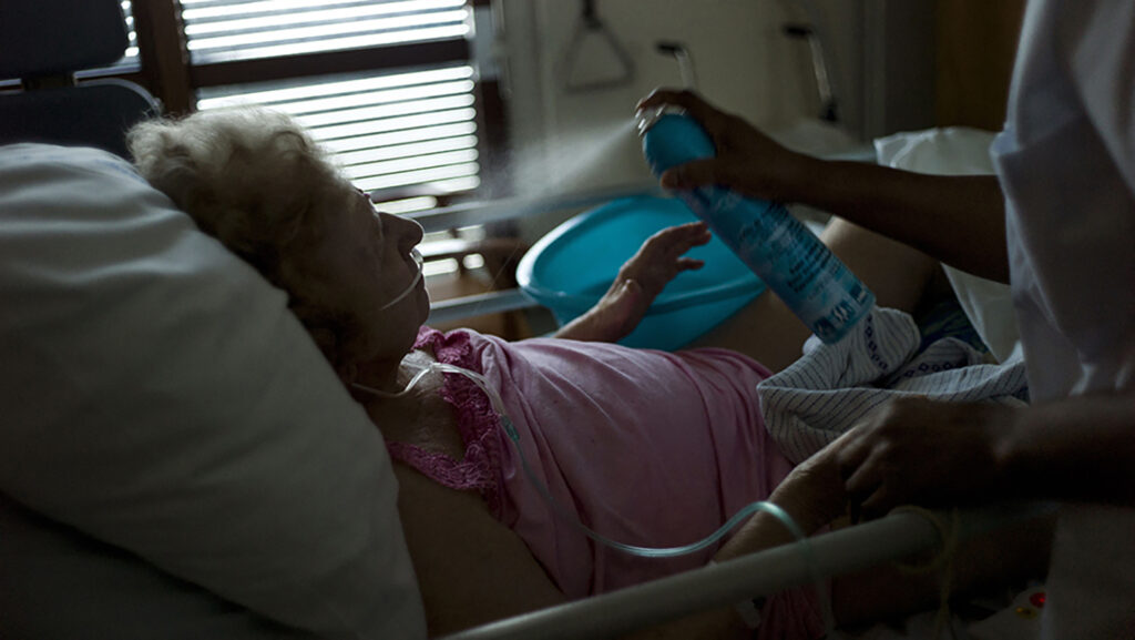 Foto einer alten Frau im Krankenhaus, die mit einem Wasserspray gekühlt wird.